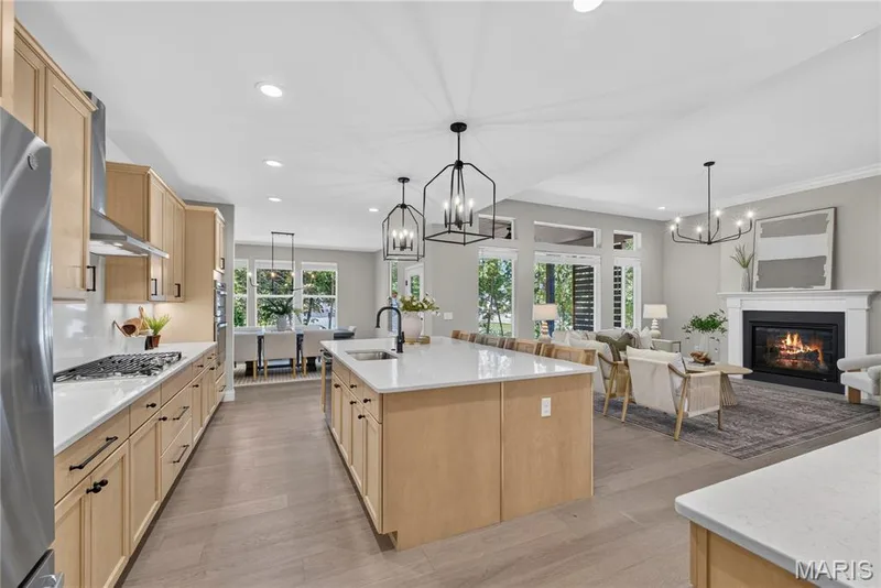 Open-concept living space with a kitchen island, wood-finish flooring, and a fireplace with a mantel — 128 Royal Troon Drive, Dardenne Prairie, MO 63368