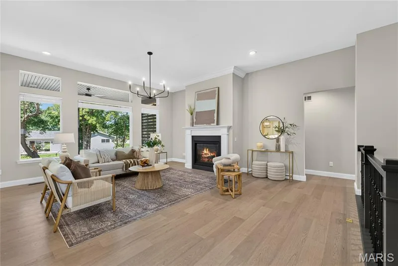 Spacious living area featuring high ceilings, wood-finish flooring, a fireplace with a white mantel, and expansive windows — 128 Royal Troon Drive, Dardenne Prairie, MO 63368