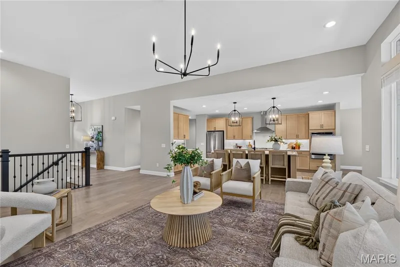 Open-concept living space featuring wood-finish flooring, a contemporary chandelier, and a kitchen with stainless steel appliances, light wood-finish cabinetry, and an island with pendant lighting — 128 Royal Troon Drive, Dardenne Prairie, MO 63368