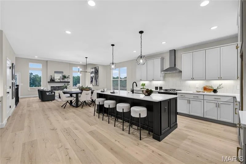 Open-concept kitchen and living area featuring wood-finish flooring, a contemporary kitchen island with seating, pendant lighting, and a fireplace with a mantel — 366 Strawberry Grove Drive, O'Fallon, MO 63376