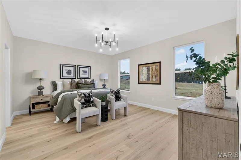 Primary bedroom featuring light wood-finish flooring, a contemporary chandelier, two large windows, and neutral wall tones — 366 Strawberry Grove Drive, O'Fallon, MO 63376
