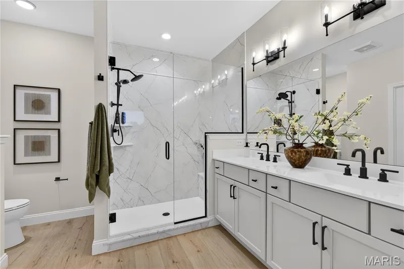 Primary Bathroom with double vanity with white cabinetry, matte black fixtures, and a spacious walk-in shower featuring a glass enclosure and marble-look tile surround — 366 Strawberry Grove Drive, O'Fallon, MO 63376