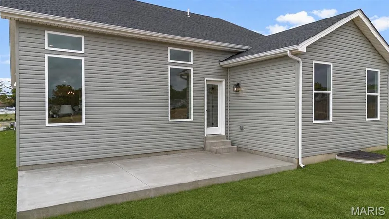 Rear exterior featuring light grey horizontal siding, a concrete patio, and a shingled roof — 366 Strawberry Grove Drive, O'Fallon, MO 63376