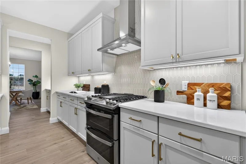 Modern kitchen featuring white shaker-style cabinetry with gold-tone hardware, white countertops, and a full-height geometric tile backsplash — 369 Strawberry Grove Drive, O'Fallon, MO 63376