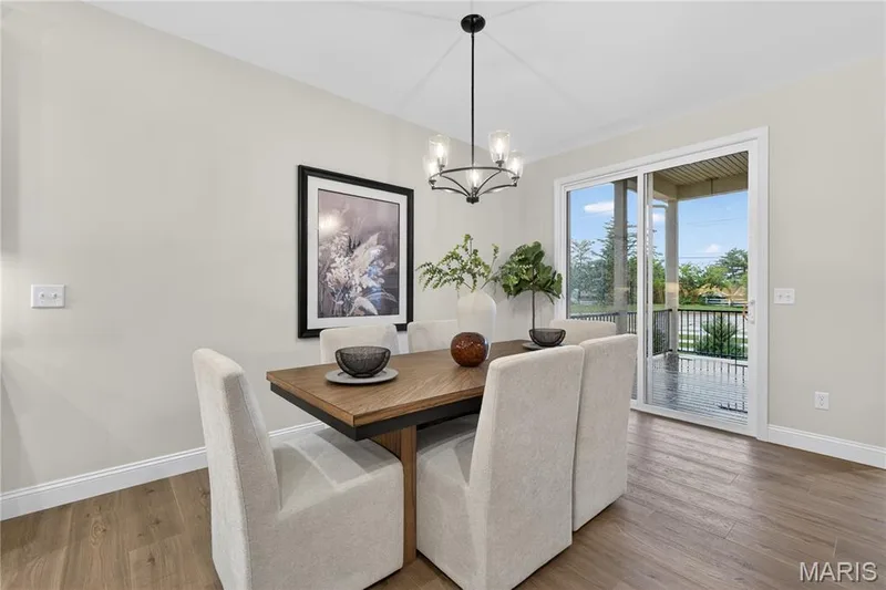 Dining area featuring wood-finish flooring, a contemporary chandelier, and a sliding glass door opening to an outdoor patio with a black railing — 369 Strawberry Grove Drive, O'Fallon, MO 63376