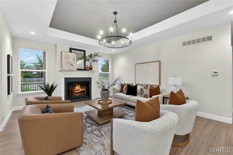 Living area featuring a fireplace with white mantel, tray ceiling with recessed lighting, wood-finish flooring, and multiple windows — 369 Strawberry Grove Drive, O'Fallon, MO 63376