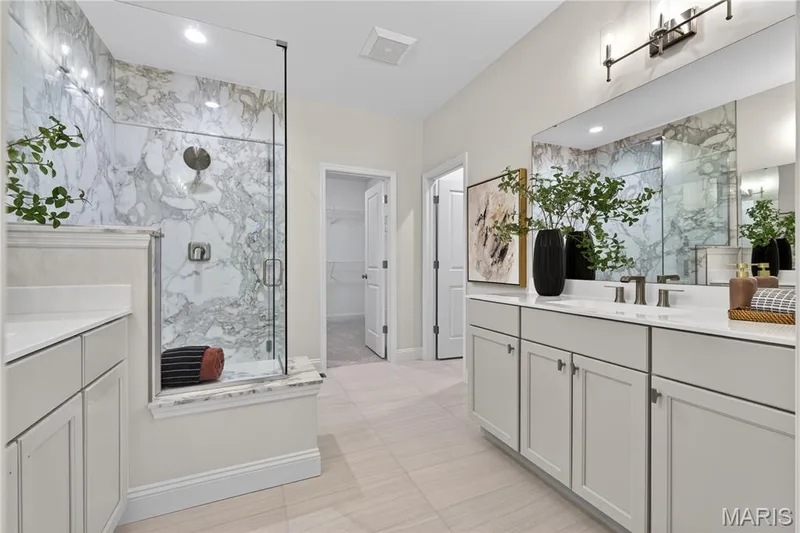 Primary bathroom featuring a frameless glass shower enclosure with marble-patterned tile, dual vanity with undermount sinks, and light-toned tile flooring — 369 Strawberry Grove Drive, O'Fallon, MO 63376