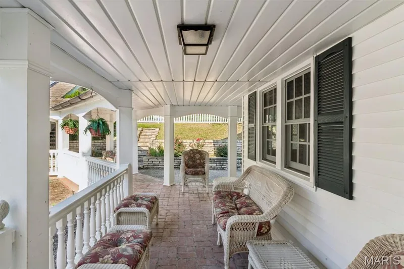Covered porch featuring a brick-finish floor, white balusters, beadboard ceiling, and exterior lighting — 2333 Ossenfort Road, Wildwood, MO 63038