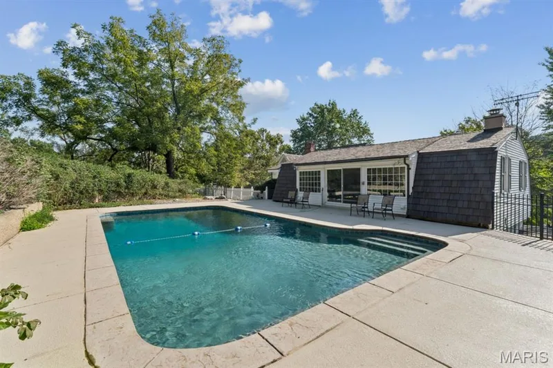 In-ground swimming pool with integrated steps, expansive concrete decking, and adjacent exterior building with large sliding glass doors — 2333 Ossenfort Road, Wildwood, MO 63038