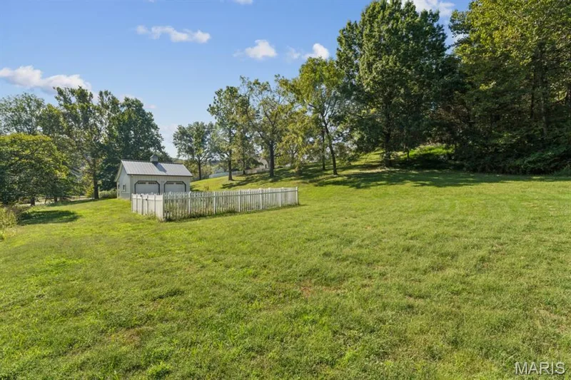 Expansive grassy area featuring a two-car garage with roll-up doors, a white picket fence enclosure, and mature trees — 2333 Ossenfort Road, Wildwood, MO 63038