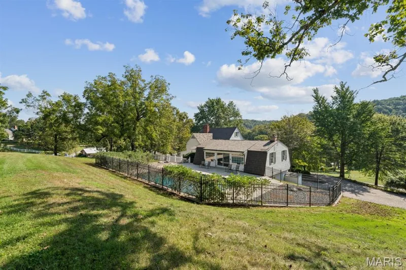 Expansive outdoor living area featuring a fenced swimming pool, spacious patio, mature trees, and a sloped lawn — 2333 Ossenfort Road, Wildwood, MO 63038