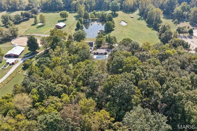 Sprawling acreage featuring mature tree-lined grounds, multiple outbuildings with metal roofing, a serene pond, and lush pastureland ideal for equestrian or agricultural pursuits — 2333 Ossenfort Road, Wildwood, MO 63038