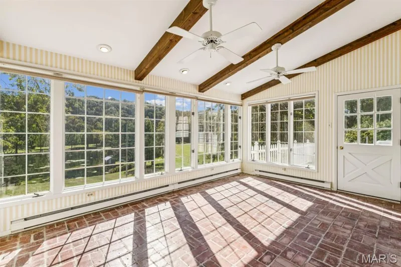 Sunlit sunroom showcasing expansive multi-pane windows, exposed wood beam ceiling detail, recessed and ceiling fan lighting, and geometric tile flooring in warm earth tones — 2333 Ossenfort Road, Wildwood, MO 63038