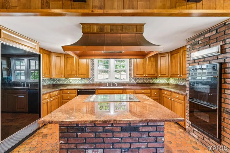 Kitchen featuring wood cabinetry, a central island with a brick base and cooktop, integrated double ovens, and hexagonal tile flooring — 2333 Ossenfort Road, Wildwood, MO 63038