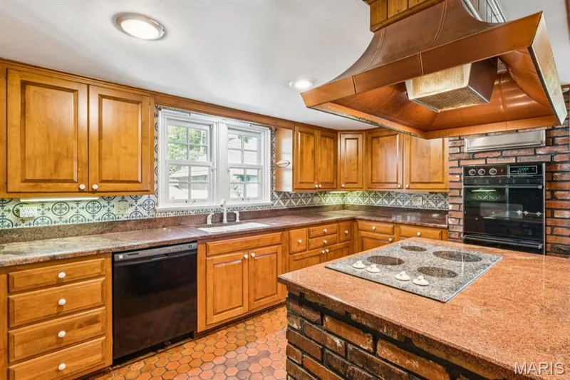Warm wood cabinetry, stone countertops, integrated cooktop, built-in oven, and brick detailing — 2333 Ossenfort Road, Wildwood, MO 63038