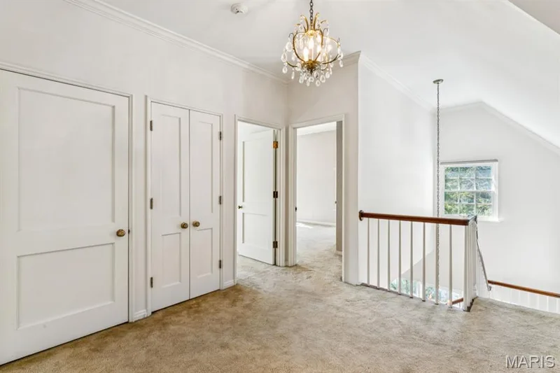 Carpeted hallway with a brass chandelier, a window with exterior visibility, white panel doors, and a wood handrail — 2333 Ossenfort Road, Wildwood, MO 63038