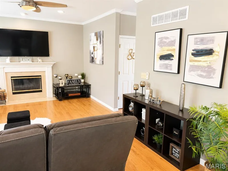 Living area featuring wood-finish flooring, a fireplace with a white mantel, and crown molding — 1126 Manor Cove Drive, St Charles, MO 63304