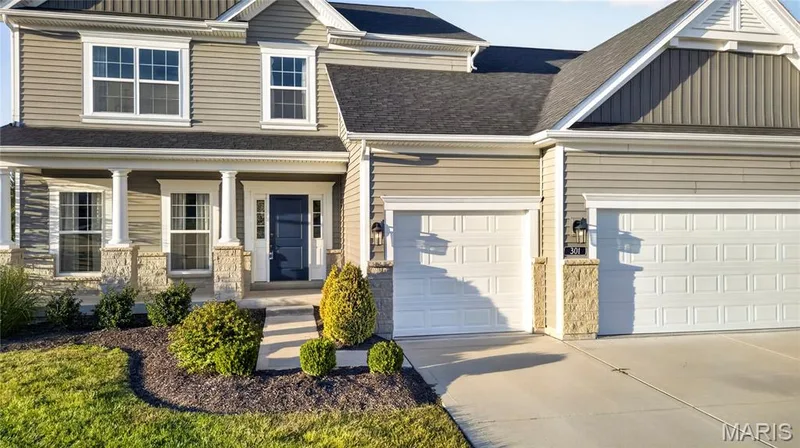 Siding exterior with stone accents, covered front porch with columns, dark paneled front door, attached three-car garage, and concrete driveway — 301 Healthy Way, St Charles, MO 63304