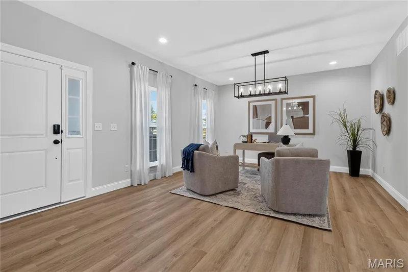 A welcoming foyer opens to a bright home office, featuring tall windows that fill the space with natural light. Wood-look flooring, neutral finishes, recessed lighting, and a striking black chandelier create an inviting setting for work or reading. — 301 Healthy Way, St Charles, MO 63304