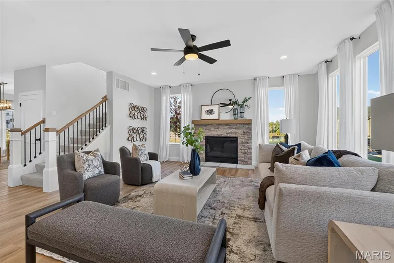 Light-filled great room featuring a stone-surround fireplace, wood mantel, and expansive windows. — 301 Healthy Way, St Charles, MO 63304