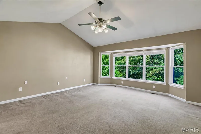 Vaulted ceiling primary Bedroom Suite featuring a wide bay window, neutral wall tones, grey carpeting, and a ceiling fan with integrated lighting and massive walk in closet — 1103 Panda Court, Wentzville, MO 63385