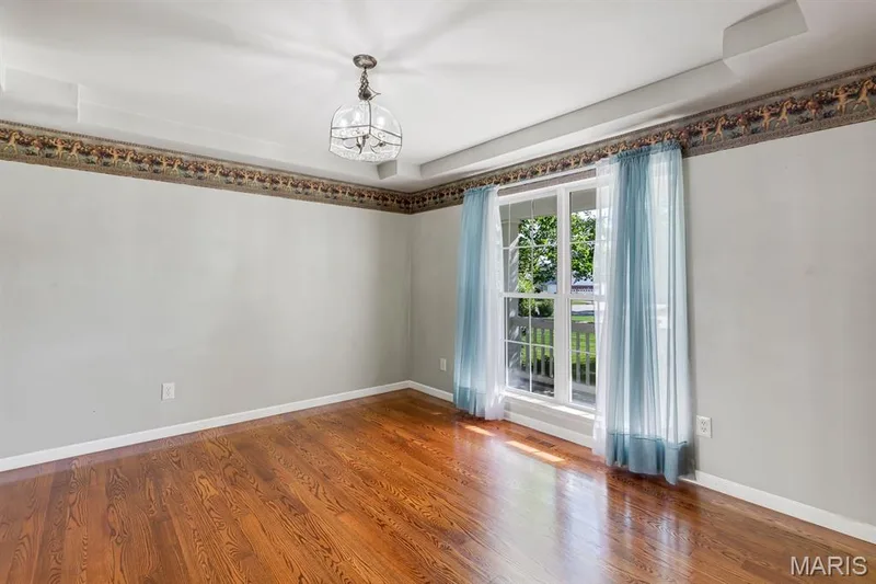 Hardwood flooring throughout, recessed ceiling with a central chandelier, and a large window providing ample natural light — 1103 Panda Court, Wentzville, MO 63385
