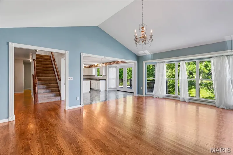 Vaulted ceiling living space featuring wood-finish flooring, a decorative chandelier, and a wall of windows — 1103 Panda Court, Wentzville, MO 63385