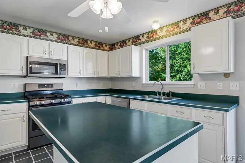 Kitchen featuring white cabinetry, a central island, stainless steel appliances, a double basin sink, and a window overlooking exterior greenery — 1103 Panda Court, Wentzville, MO 63385