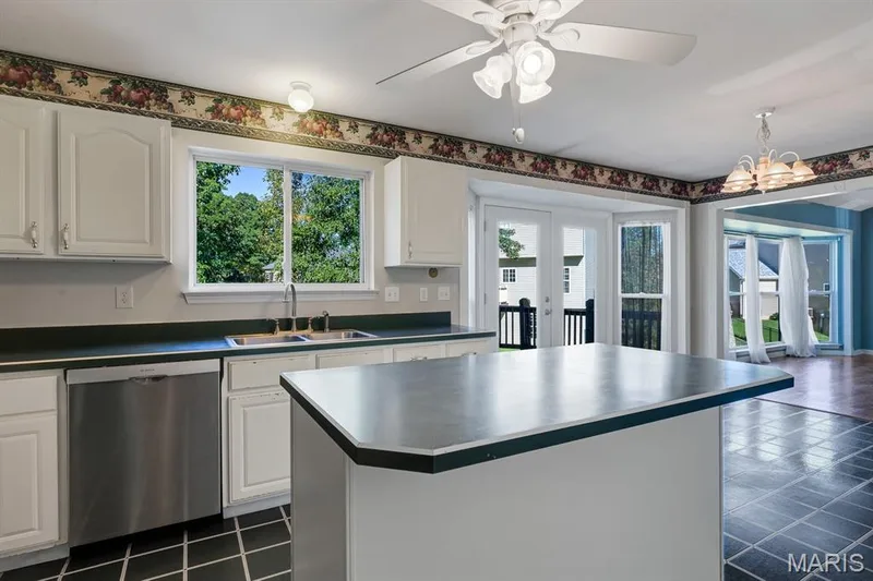 Kitchen featuring an island, white cabinetry, dark countertops, and a stainless steel dishwasher — 1103 Panda Court, Wentzville, MO 63385