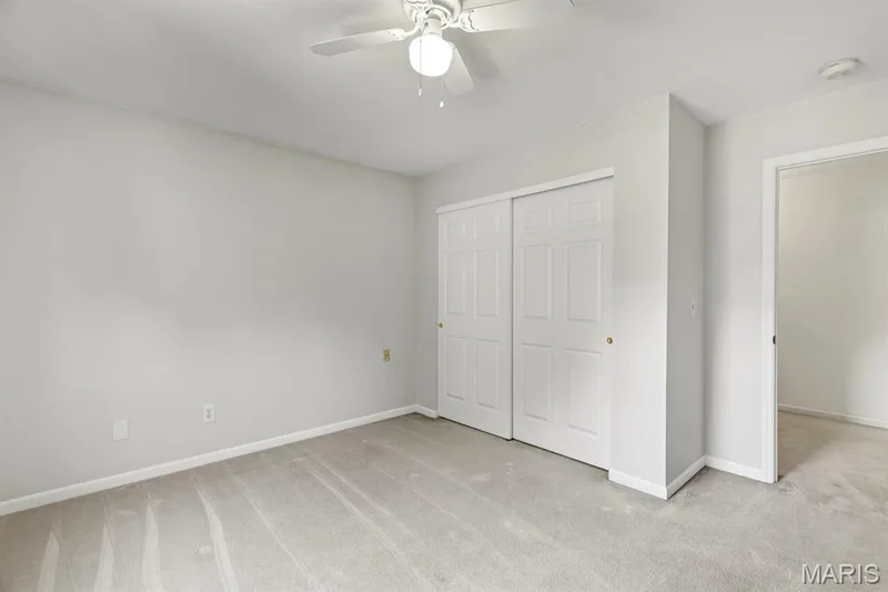 Neutral-toned room featuring a ceiling fan with integrated lighting, a double-door sliding closet with panel detailing, and light gray wall-to-wall carpeting — 1103 Panda Court, Wentzville, MO 63385
