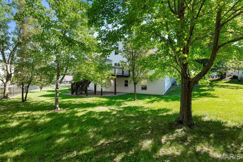 Lush green lawn with mature trees and a multi-level deck featuring a concrete patio — 1103 Panda Court, Wentzville, MO 63385