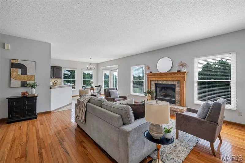 Living area featuring wood-finish flooring, a brick fireplace with a wood mantel, and multiple windows — 195 England Drive, O'Fallon, MO 63366