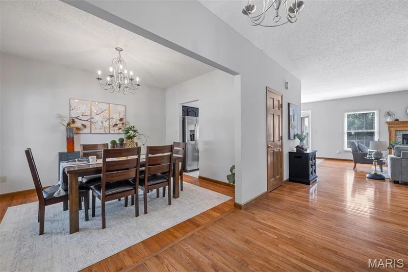 Open-concept living area featuring rich wood-finish flooring, a dining space with an overhead chandelier, and a living room with a fireplace surround — 195 England Drive, O'Fallon, MO 63366