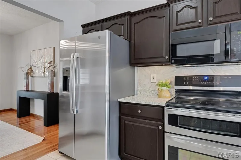 Kitchen featuring dark wood cabinetry, light granite-style countertops, and a subway tile backsplash — 195 England Drive, O'Fallon, MO 63366