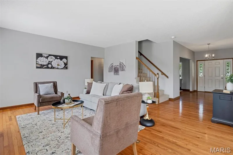 Spacious living area featuring polished wood flooring, light gray wall tones, a carpeted staircase with wood railing, and a front entry with double doors and sidelights — 195 England Drive, O'Fallon, MO 63366