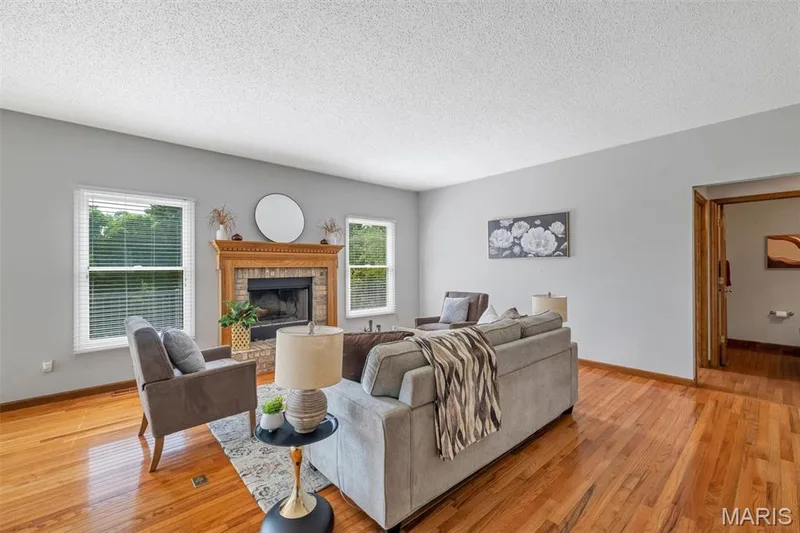 Living space featuring wood-finish flooring, a brick fireplace with an ornate wood mantel, light gray walls, and white-trimmed windows — 195 England Drive, O'Fallon, MO 63366