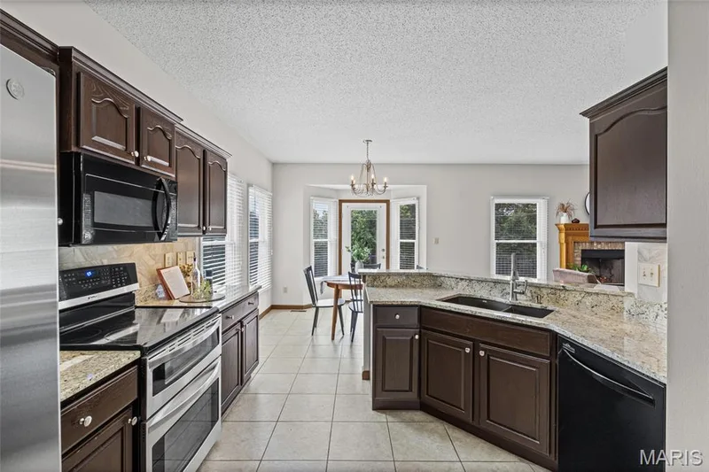 Kitchen featuring dark wood cabinetry, light-toned granite countertops, and stainless steel appliances — 195 England Drive, O'Fallon, MO 63366