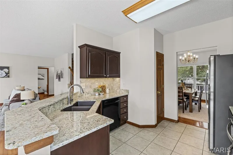 Kitchen featuring granite countertops, a double basin sink with a gooseneck faucet, dark wood cabinetry, and tile flooring — 195 England Drive, O'Fallon, MO 63366