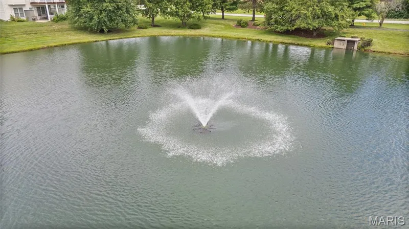 Tranquil pond featuring a central fountain, surrounded by manicured green space and mature trees — 195 England Drive, O'Fallon, MO 63366