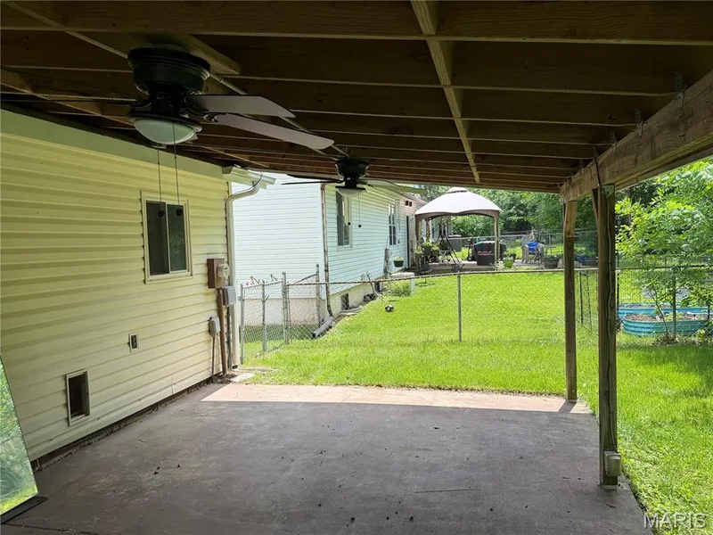 Covered patio with a concrete surface, exposed wood ceiling joists, and two attached ceiling fans — 2505 Ambelwood Lane, O'Fallon, MO 63368