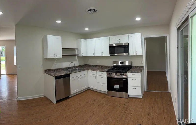 White cabinetry with stainless steel hardware, stainless steel appliance suite, dark patterned countertops, wood-finish flooring, and recessed lighting — 2505 Ambelwood Lane, O'Fallon, MO 63368