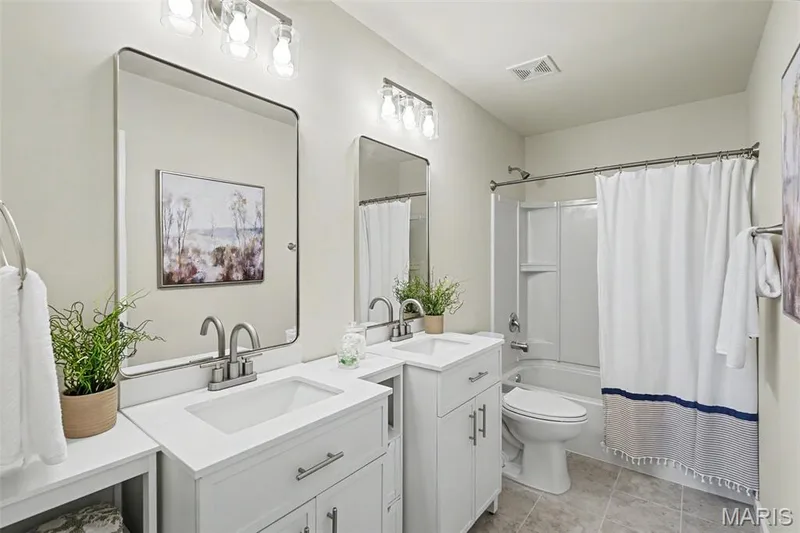 Renovated primary bath with ceramic tile flooring, new vanities, mirrors, lighting, and an elongated commode — 18 Sonnet Way Court, Wentzville, MO 63385