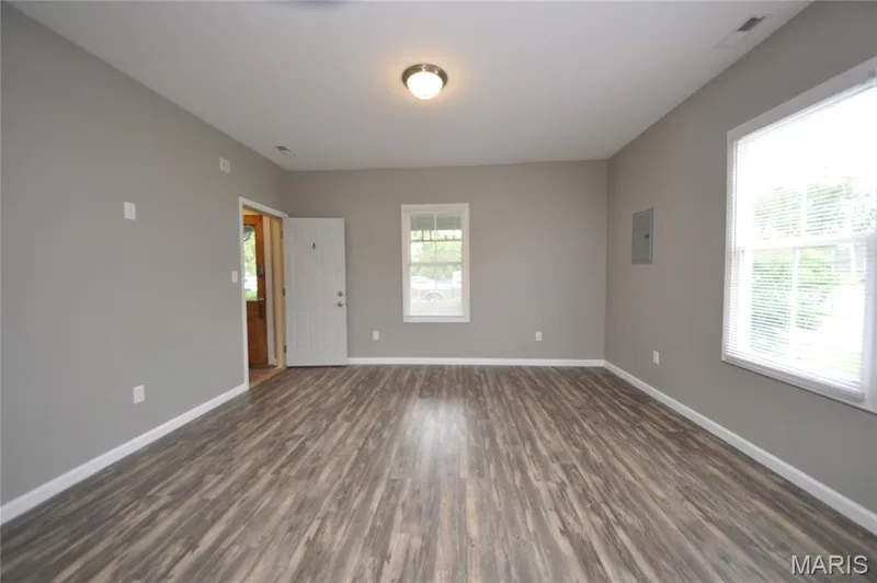 Spacious living area featuring wood-finish flooring, neutral gray walls, white trim, and ample natural light from multiple windows — 502 S Linn Avenue, Wentzville, MO 63385