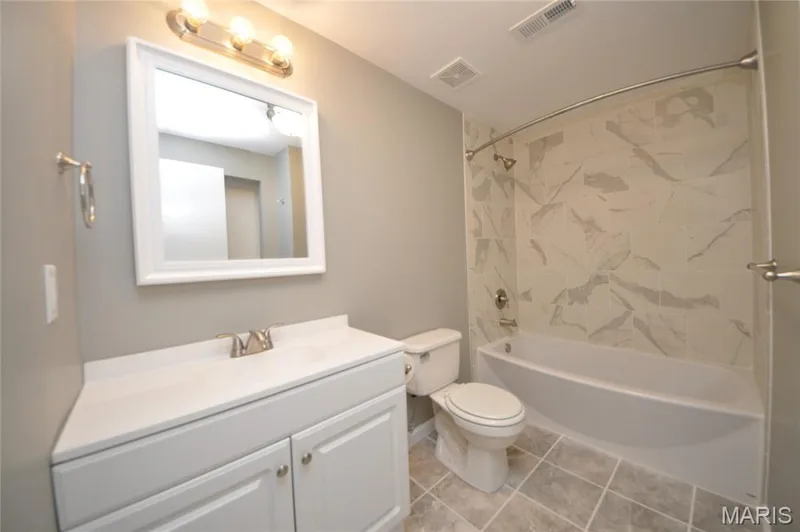 Bathroom featuring a white vanity with integrated sink, brushed nickel faucet, a framed mirror, and overhead lighting — 502 S Linn Avenue, Wentzville, MO 63385