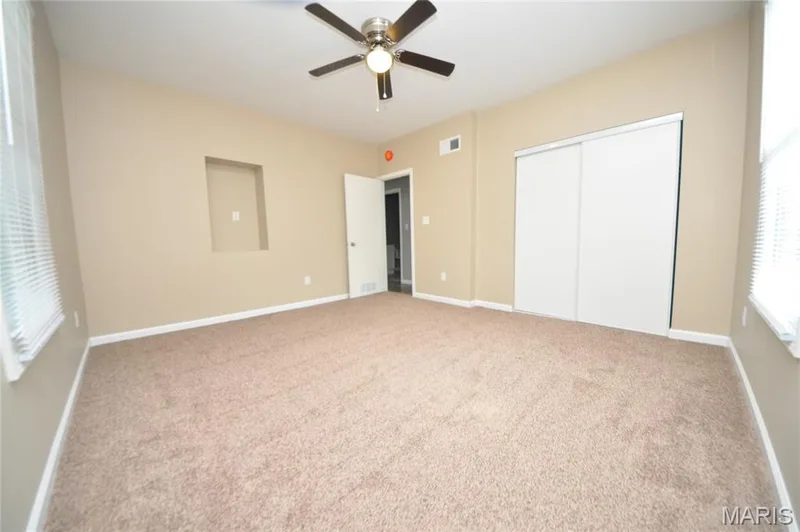 Spacious room featuring neutral carpeting, a ceiling fan, sliding closet doors, and an integrated wall niche — 502 S Linn Avenue, Wentzville, MO 63385