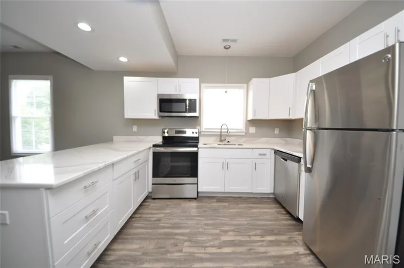 Modern kitchen featuring white shaker cabinetry, stainless steel appliances, marble-look countertops, and wood-finish flooring — 502 S Linn Avenue, Wentzville, MO 63385