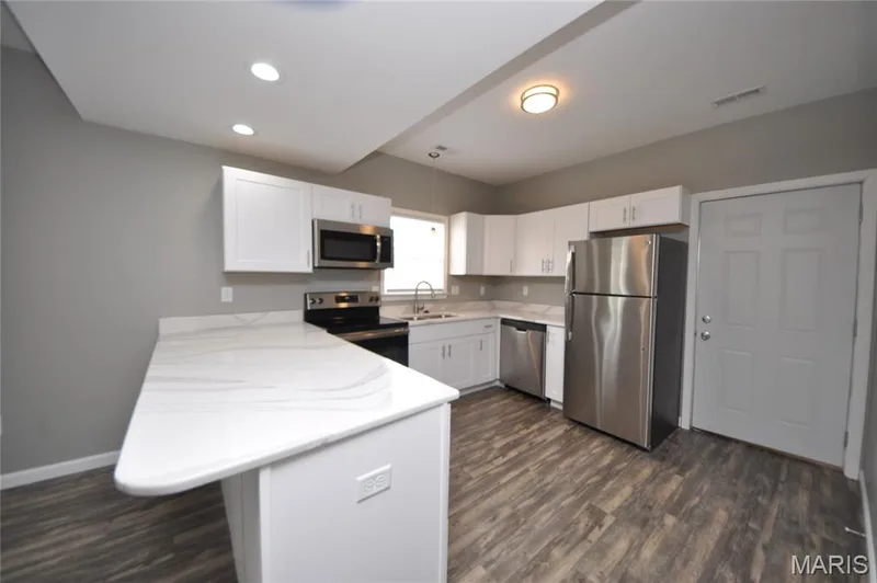 Kitchen featuring an extended island with white countertops, stainless steel appliances, white cabinetry, and wood-finish flooring — 502 S Linn Avenue, Wentzville, MO 63385
