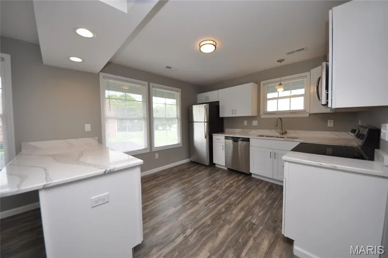 Kitchen featuring white cabinetry, a kitchen island with a light-toned countertop, stainless steel appliances, and wood-finish flooring — 502 S Linn Avenue, Wentzville, MO 63385