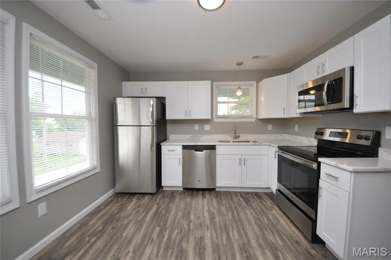 Modern kitchen featuring white cabinetry, light-toned countertops, and stainless steel appliances including a refrigerator, dishwasher, oven, and microwave — 502 S Linn Avenue, Wentzville, MO 63385