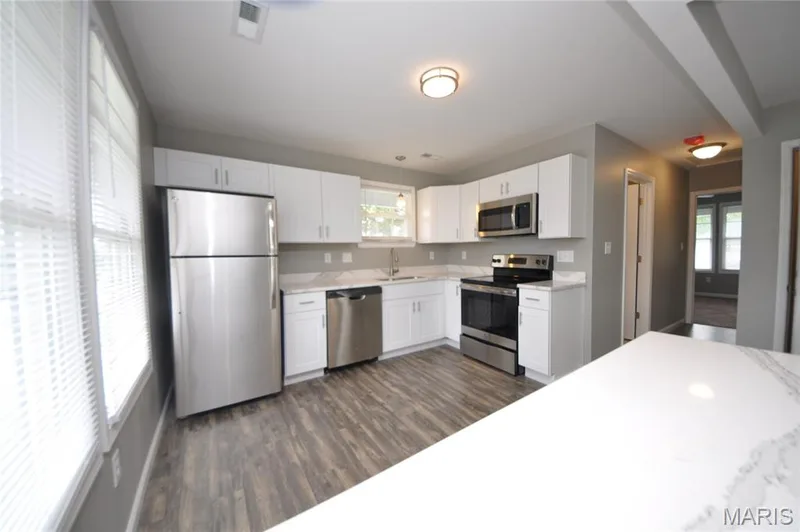 Modern kitchen featuring white cabinetry, stainless steel appliances, light-toned countertops, wood-finish flooring, and recessed lighting — 502 S Linn Avenue, Wentzville, MO 63385